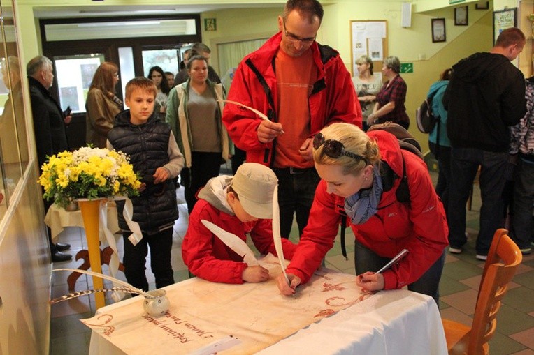 Katarzyna i Jan Kozieł z synem Konradem podpisują się gęsim piórem na dokumencie upamiętniającym skoczowską grę miejską