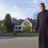 Ks. rektor Piotr Brzeski na tle jednego z budynków seminarium w Brzuchowicach; po lewej pomnik Jana Pawła II