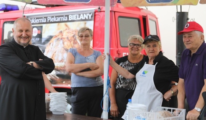 Strażacka ekipa z proboszczem przy kuchni polowej z grochówką