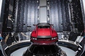 Ten sportowy samochód Tesla Roadster w kolorze wiśniowym leci w kierunku Marsa  na pokładzie rakiety Falcon Heavy.