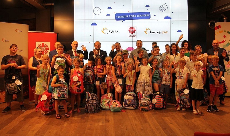 Obdarowane tornistrami dzieci ze swoimi rodzicami, dyrektorami Caritas z Bielska-Białej i Katowic, szefostwem Jastrzębskiej Spółki Węglowej i pracownikami Fundacji JSW.