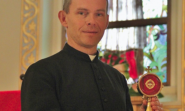 Ks. Kmak z relikwiarzem i wizerunek patrona parafii na witrażu.
