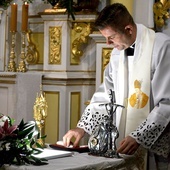 Ks. Marcin Zawada wkładający relikwie do relikwiarzy.