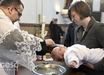 Ks. Julian Nastałek polewający wodą Kacpra trzymanego przez matkę chrzestną.