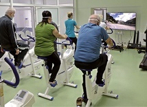 Rehabilitacja pocovidova w Głuchołazach. Wśród aktywności jest jazda na rowerze przy obserwowaniu dynamicznie zmieniających się krajobrazów na ekranie telewizora.