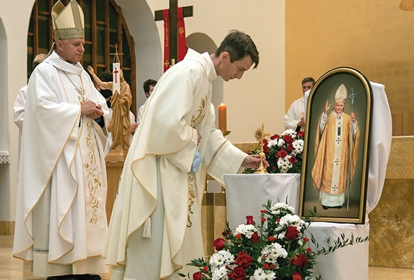 Proboszcz ks. Jacek Orszulak składa relikwiarz obok obrazu papieża Polaka.