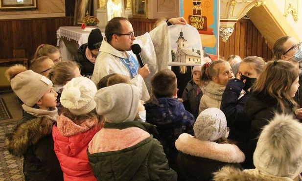 Ks. Marcin Samek prezentuje dzieciom zdjęcie kościoła św. Jakuba w Rzykach, znalezione w skrzyni tajemnic.