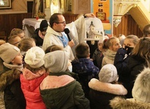 Ks. Marcin Samek prezentuje dzieciom zdjęcie kościoła św. Jakuba w Rzykach, znalezione w skrzyni tajemnic.
