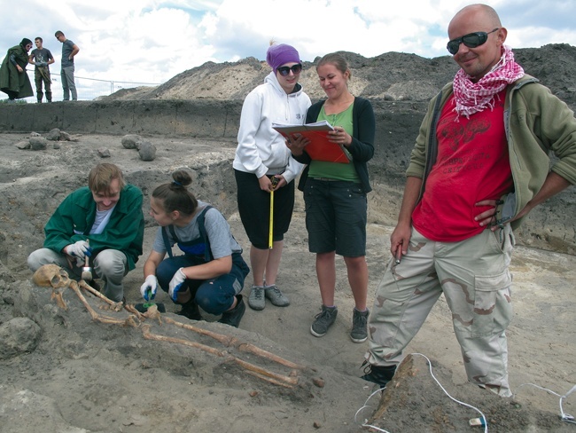 O tym, jak archeologia traktuje pochówki i jak się je dokumentuje, mówił uczestnikom letniej szkoły kierownik badań Maciej Trzeciecki z Instytutu Archeologii i Etnologii PAN (z prawej). Kucają Ada i Mateusz