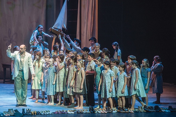 Buty dzieci na pierwszym planie sceny z musicalu „Korczak” przypominają, jak zginęli jego bohaterowie. Tomasz Steć (dr Korczak) z dziecięcym zespołem operowym