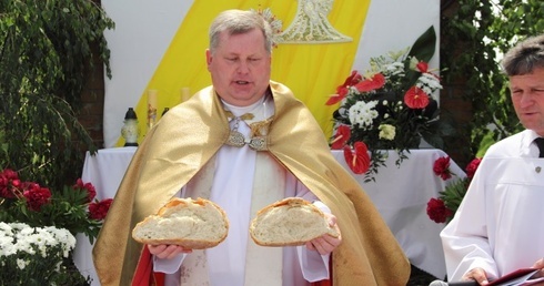 Proboszcz ks. Zdzisław Madzio dzieli chleb przy czwartym ołtarzu procesji Bożego Ciała