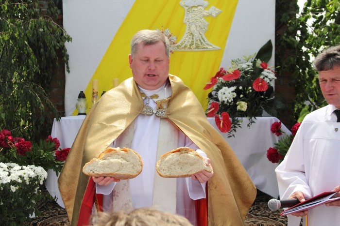 Proboszcz ks. Zdzisław Madzio dzieli chleb przy czwartym ołtarzu procesji Bożego Ciała