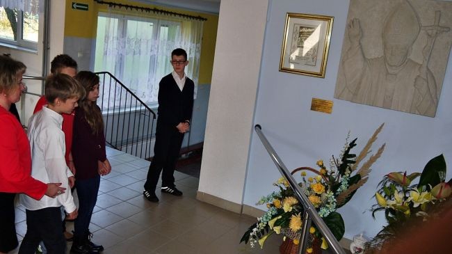 Uczniowie gimnazjum przed tablicą i popiersiem upamiętniającym nadanie szkole papieskiego imienia