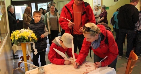 Katarzyna i Jan Kozieł z synem Konradem podpisują się gęsim piórem na dokumencie upamiętniającym skoczowską grę miejską