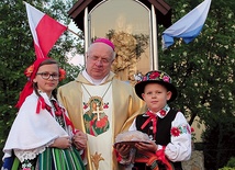  Bp Józef Zawitkowski wraz z dziećmi ubranymi w stroje łowickie przy maryjnej kapliczce