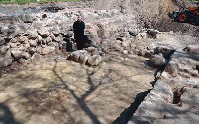 Ks. Henryk Romanik w środku odkrytego prezbiterium przy grupie kamieni, które z dużym prawdopodobieństwem są fundamentem głównego ołtarza