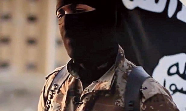 Bojownik Państwa Islamskiego  z flagą organizacji w tle 