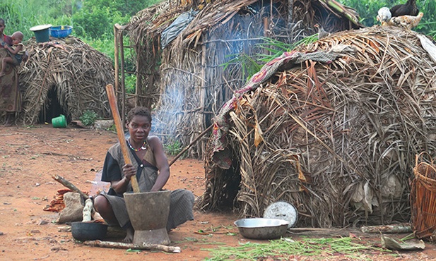 Pigmejka przed swoją chatą z palmowych liści i patyków. Właśnie ubija maniok, z którego przygotuje posiłek foto Beata Zajączkowska