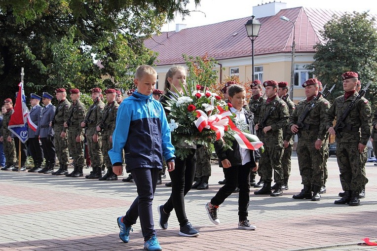 Delegacja uczniów niesie wiązankę kwiatów pod pomnik na pl. Kościuszki