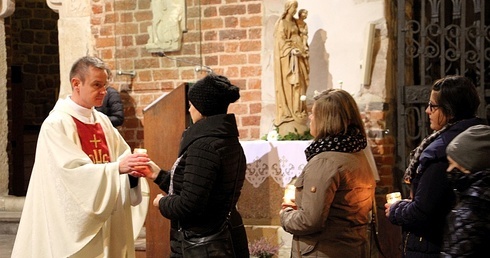 Rodzice przekazują ks. Piotrowi Nowakowi zapalone znicze, których płomień symbolizuje utracone dziecko