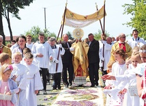 Kapłan z Najświętszym Sakramentem kroczy  po kwietnym kobiercu.