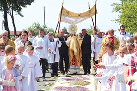 Kapłan z Najświętszym Sakramentem kroczy  po kwietnym kobiercu.