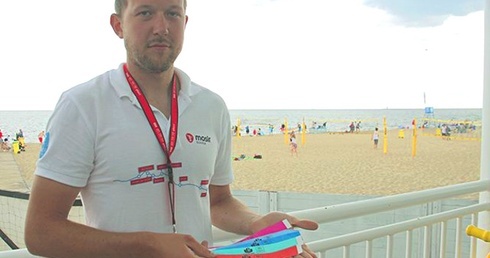 Mateusz Żylewicz pokazuje darmowe opaski, które można otrzymać od ratowników na gdańskich plażach.