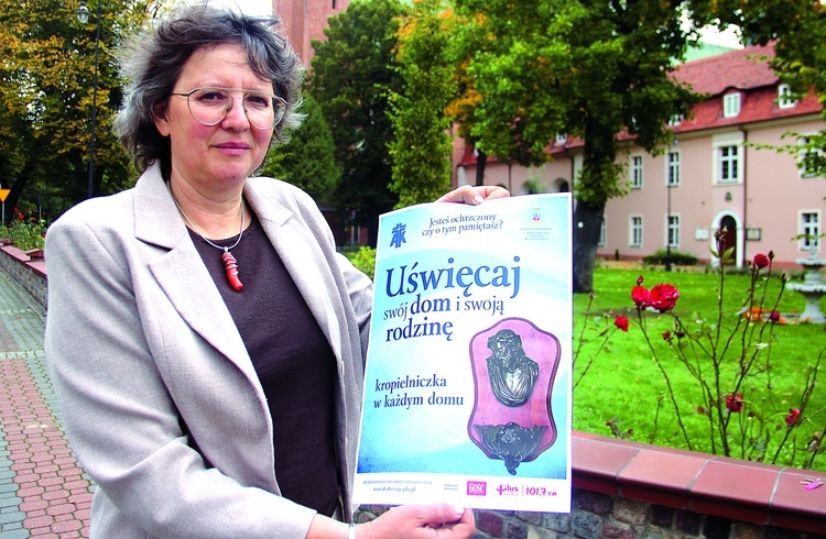 	Joanna Olbert, prezes DIAK AG, prezentuje plakat promujący inicjatywę „Uświęcaj swój dom i swoją rodzinę”.