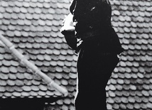 Kominiarz artysta stojący na kominie wentylacyjnym bez zabezpieczenia i butów.
