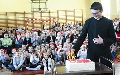 Ksiądz Damian Warzecha zapala świeczki  na jubileuszowym torcie.
