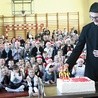 Ksiądz Damian Warzecha zapala świeczki  na jubileuszowym torcie.