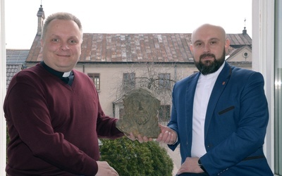 Ks. Robert Kowalski (z lewej) i ks. Damian Drabikowski, wicedyrektor radomskiej Caritas, pokazują znaleziony podczas remontu kaplicy stary żeliwny odlew głowy Chrystusa. W tle dawna kaplica, obecnie magazyn radomskiej organizacji charytatywnej