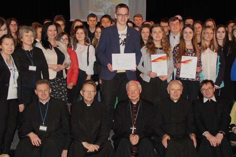 Siedzą od lewej: ks. Marcin Rogala, ks. Jacek Kucharski, bp Adam Odzimek, ks. Stanisław Łabendowicz i ks. Mirosław Prasek, filipin. Na środku stoi Tomasz Sar, a obok z dyplomami - Emila Myrta i Martyna Sowa (z prawej)