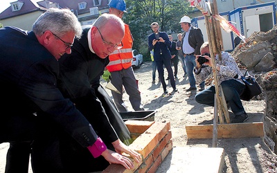 Biskup Marian Niemiec i o. Piotr Świerczok wspólnie wmurowują symboliczną cegłę.