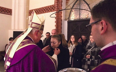 Biskup Zbigniew Kiernikowski podaje kandydatom krzyż  do ucałowania.