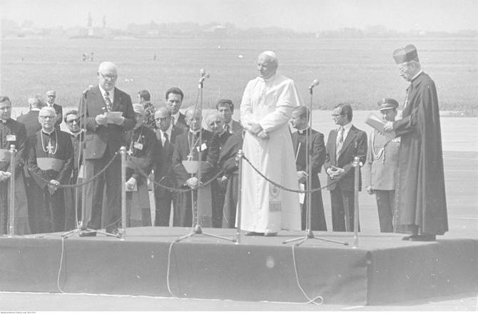 Warszawa, 2 czerwca 1979 r. Przemówienie powitalne przewodniczącego Rady Państwa PRL Henryka Jabłońskiego. Na podium widoczni również: papież Jan Paweł II, prymas Polski, kard. Stefan Wyszyński. W 1. rzędzie za podium widoczni m.in. prefekt Domu Papieskiego, bp Jacques Martin (1. na prawo od H. Jabłońskiego), abp Eduardo Martinez Somalo (3. na prawo od H. Jabłońskiego), sekretarz papieża, ks. Stanisław Dziwisz (1. na prawo od Jana Pawła II)