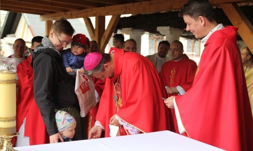 Grześ i Staś razem z tatą Jankiem wręczają bp. Romanowi Pindlowi pielgrzymią plakietkę.