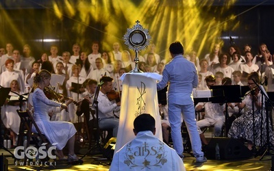 Najświętszy Sakrament otoczony gronem muzyków w blasku reflektorów.