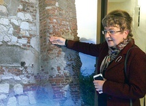 ▲	Prof. Joanna Kalaga omawia zdjęcie,  na którym widać fragmenty późnoromańskiego muru. Znajduje się on we wschodniej części obecnego kościoła.