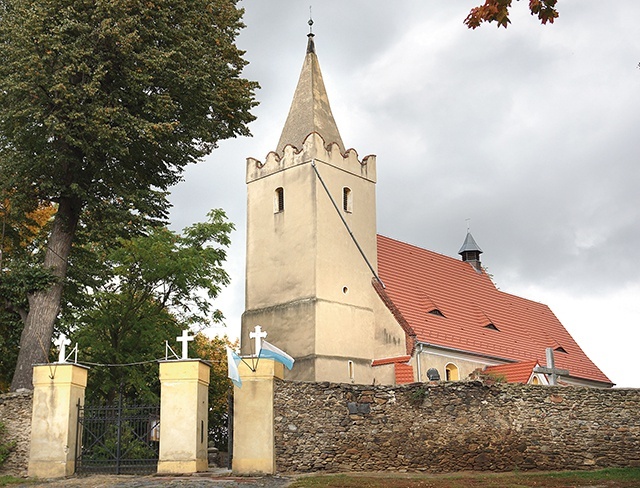 ▲	Kościół parafialny otacza mur z kamienia polnego, odłamków skalnych i cegły.