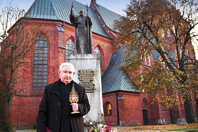 Ks. Henryk Romanik z relikwiarzem przed pomnikiem Ojca Świętego, który upamiętnia papieską wizytę z 1991 roku.