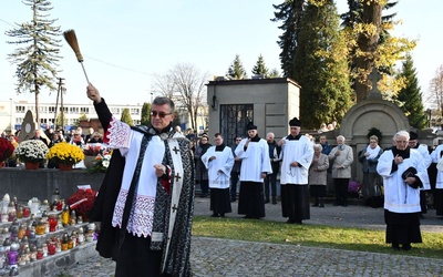 Ks. Jerzy Jurkiewicz kropi wodą święconą groby podczas procesji we Wszystkich Świętych.