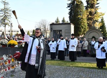 Ks. Jerzy Jurkiewicz kropi wodą święconą groby podczas procesji we Wszystkich Świętych.