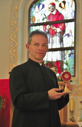Ks. Kmak z relikwiarzem i wizerunek patrona parafii na witrażu.
