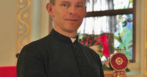 Ks. Kmak z relikwiarzem i wizerunek patrona parafii na witrażu.