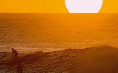 Mężczyzna surfujący na Hawajach o zachodzie słońca. 
28.01.2020 Plaża na wyspie Oahu, Stany Zjednoczone