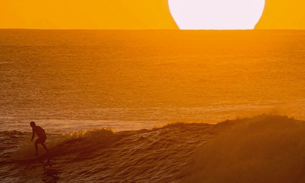 Mężczyzna surfujący na Hawajach o zachodzie słońca. 
28.01.2020 Plaża na wyspie Oahu, Stany Zjednoczone
