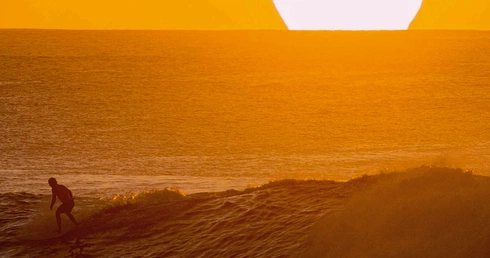 Mężczyzna surfujący na Hawajach o zachodzie słońca. 
28.01.2020 Plaża na wyspie Oahu, Stany Zjednoczone