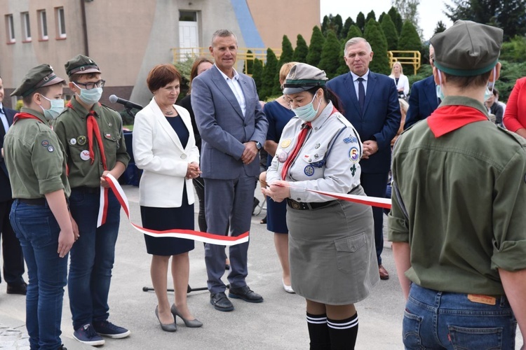 Przedstawicielka harcerzy przecina wstęgę przed tablicą pamięci.