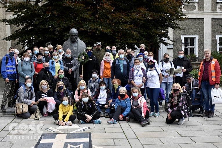 Grupowe zdjęcie pieszych pielgrzymów pod bardzkim pomnikiem św. Jana Pawła II.